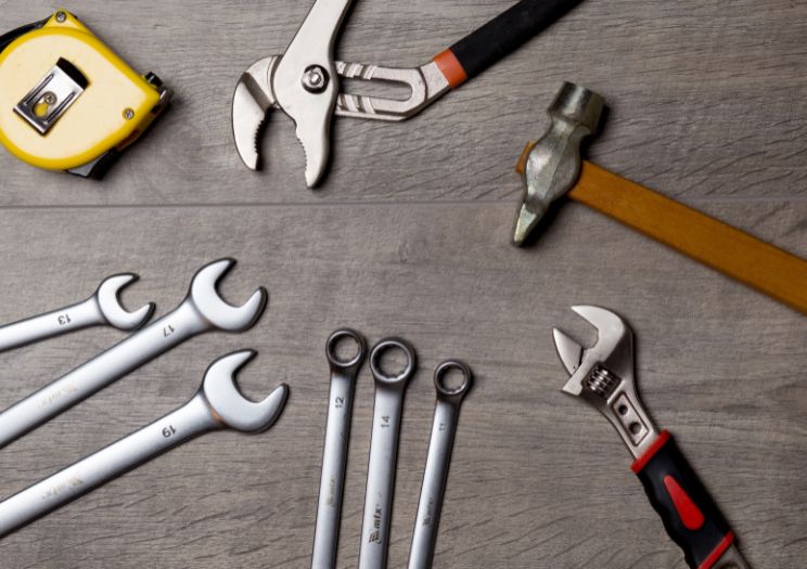An assortment of wrenches, hammers and other property repair tools lie on a desk.