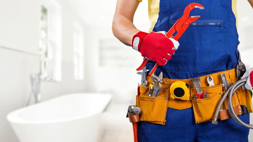 The lower half of a maintenance worker wearing a blue apron is pictured as they work on a property owner’s white bathroom, their belt in the frame.