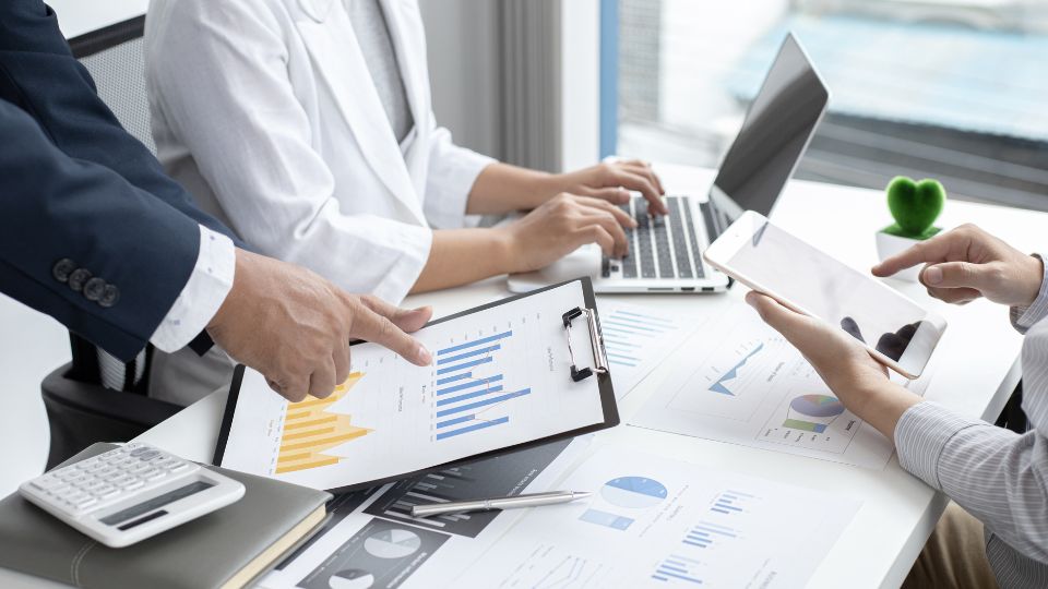 A team of property managers hands are pictured over an office desk as they go over online and written marketing data and decide on a marketing strategy.