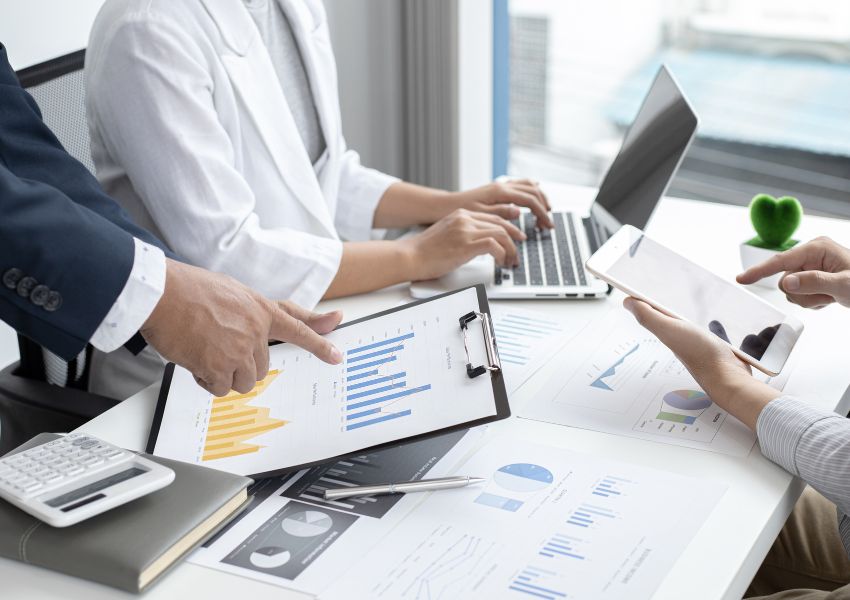 Three property managers sit at a desk in business attire as they work over graphs, figures and laptops to affirm a property marketing strategy.