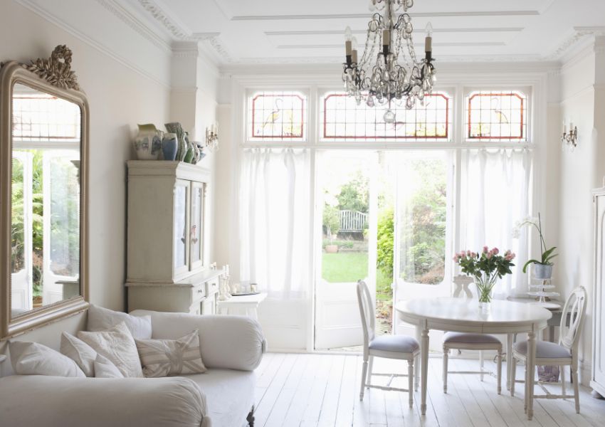 A Denton rental property living room is pictured with white and neutral tones, floor to ceiling windows and a chandelier.