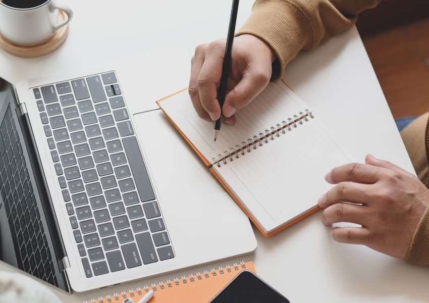 A property manager sits at a desk behind a laptop while jotting down ideas for their ad copy in a notebook.