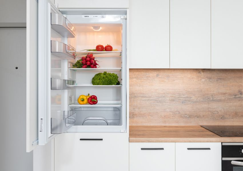 A new and clean kitchen is pictured with the fridge open and well organizes, containing only various fruits.
