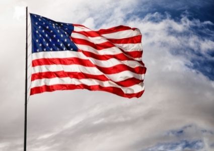 An American flag blows in the wind against a cloudy blue sky.