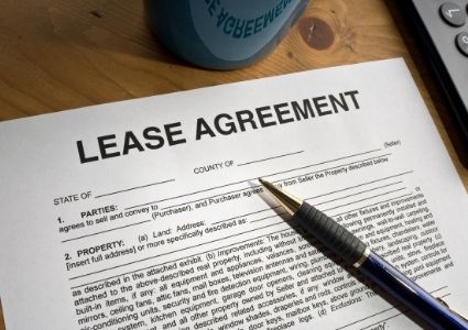 A lease agreement sits on a wooden desk, ready to be filled in with a pen.