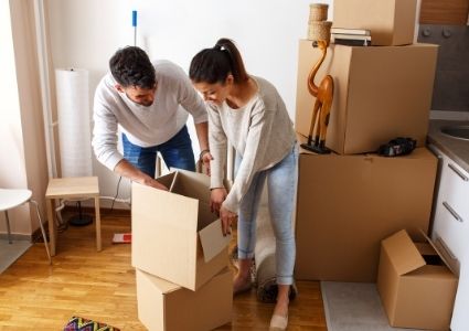 Two tenants are bent over to pack their belongings into cardboard moving boxes.